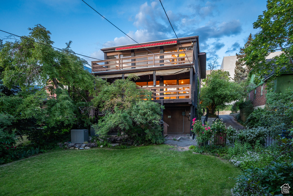 Rear view of property featuring a yard, a wooden deck, and a balcony