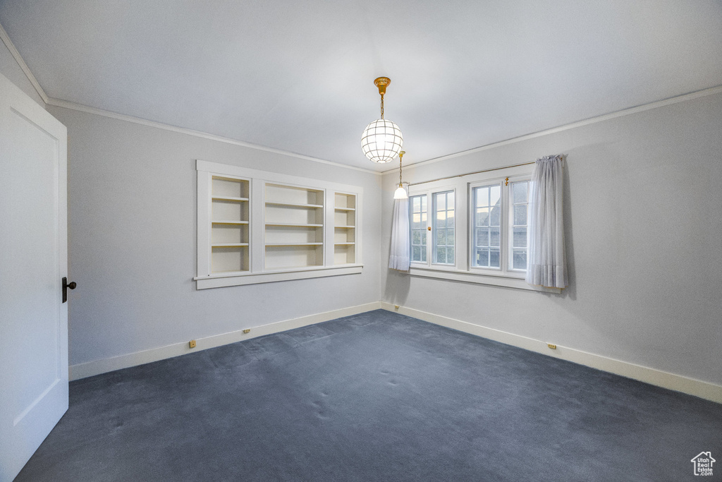 Unfurnished room featuring built in features, dark colored carpet, and ornamental molding
