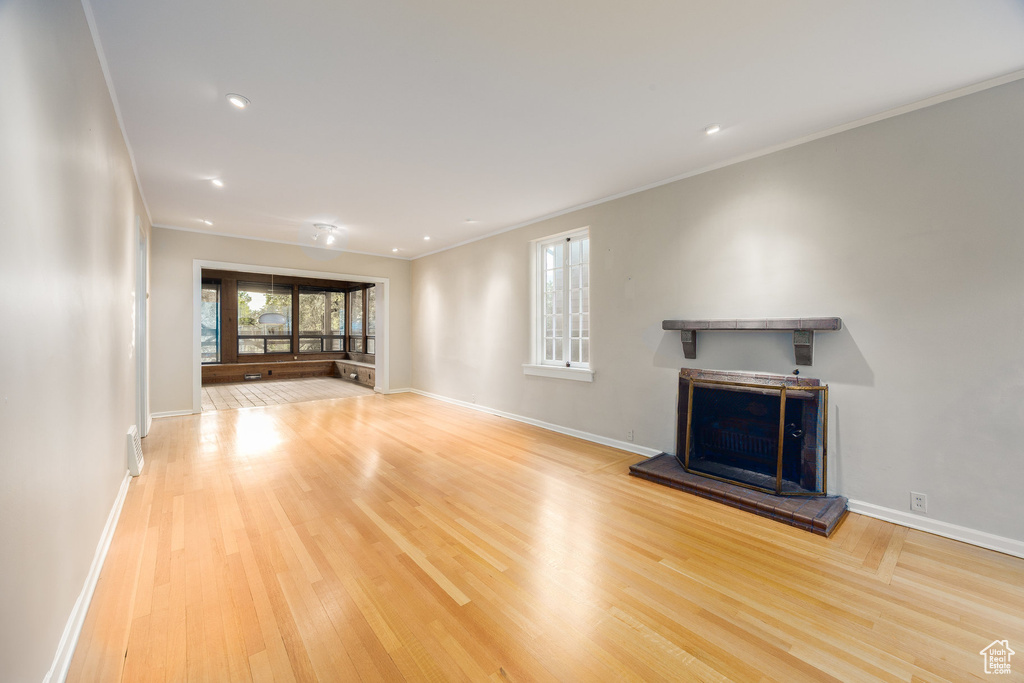 Unfurnished living room with a fireplace with raised hearth, wood finished floors, and crown molding
