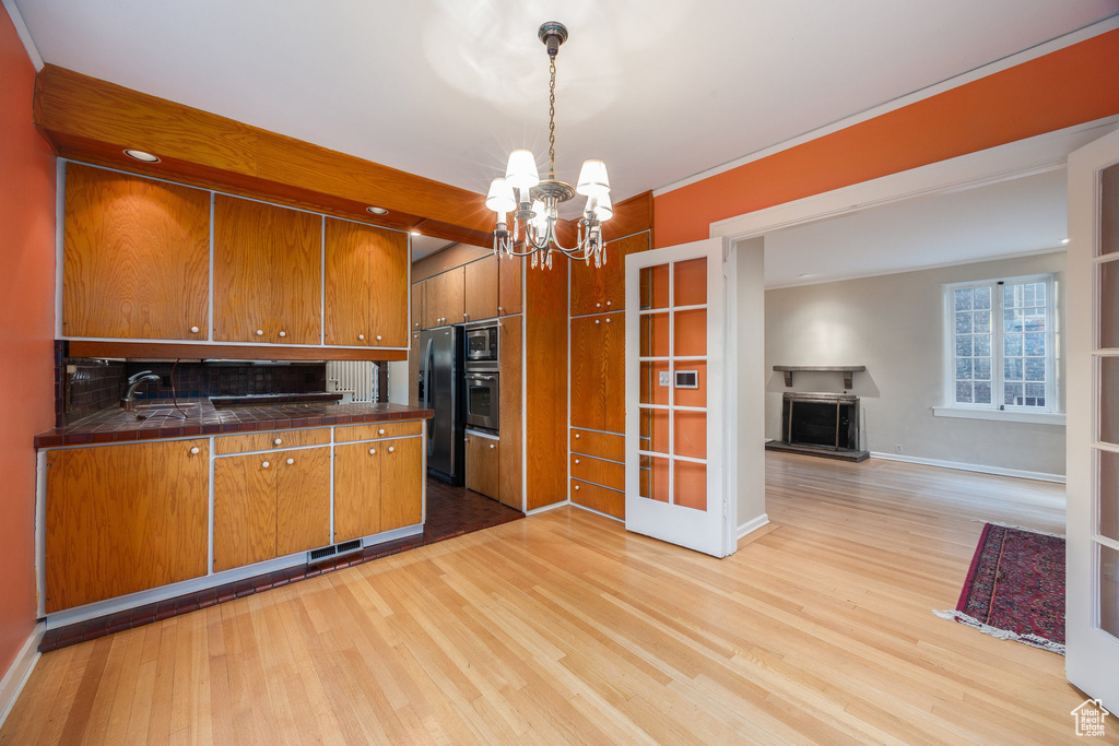 Kitchen featuring stainless steel appliances, brown cabinets, a chandelier, light wood-style floors, and tile countertops