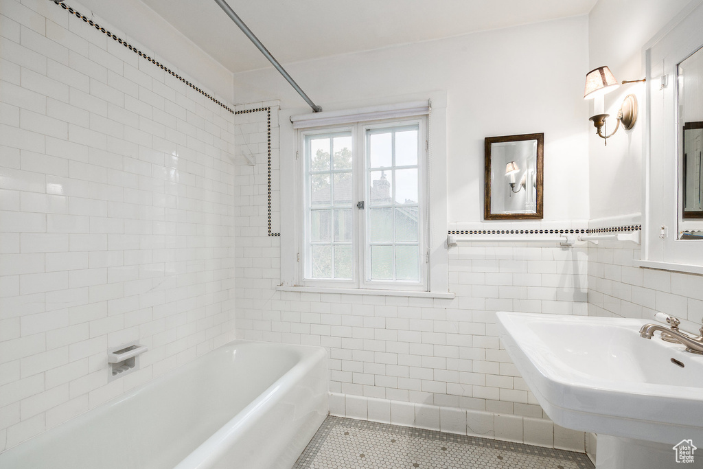 Full bath featuring a tub to relax in, tile walls, tile patterned flooring, and wainscoting