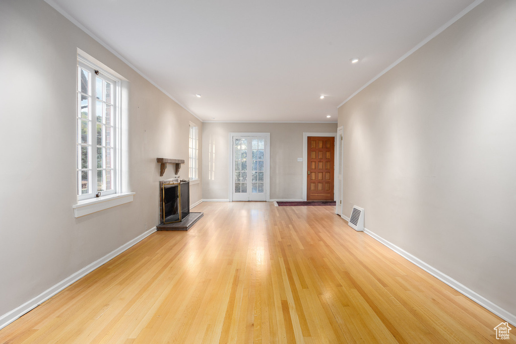 Unfurnished living room with a fireplace with raised hearth, light wood finished floors, ornamental molding, and recessed lighting