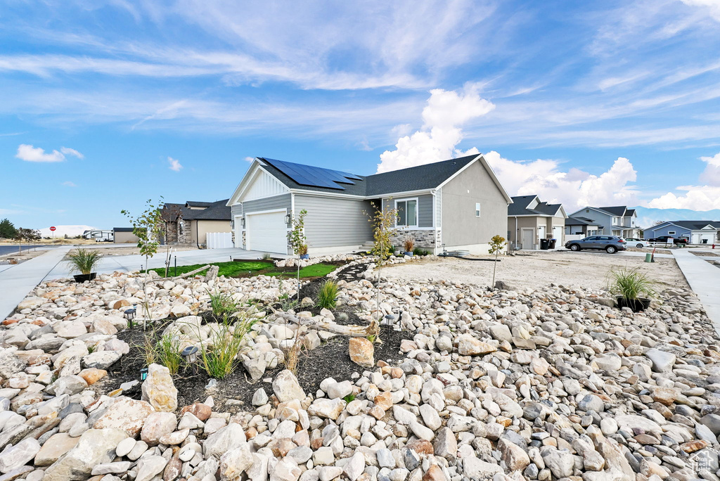 View of front of house with solar panels, an attached garage, a residential view, and driveway