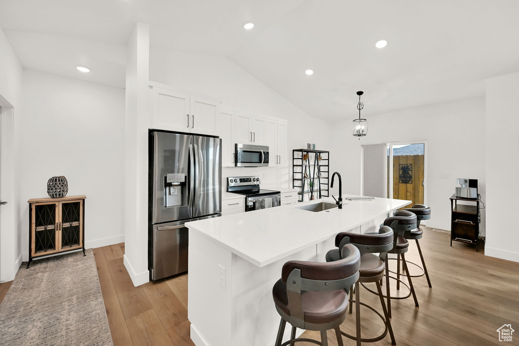 Kitchen with stainless steel appliances, light wood-style floors, a center island with sink, white cabinets, and lofted ceiling