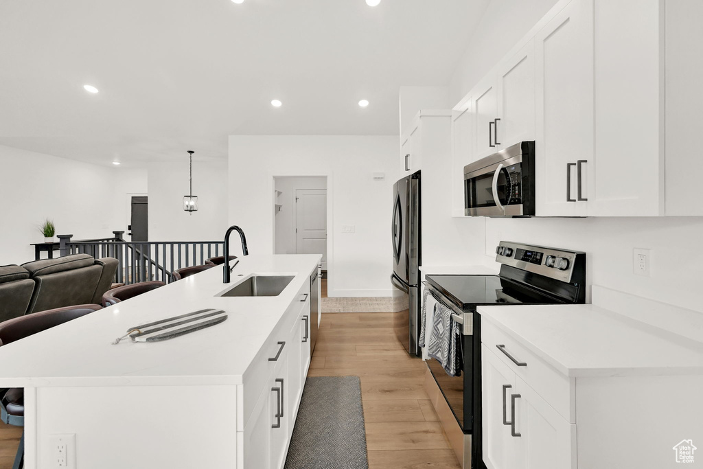 Kitchen with appliances with stainless steel finishes, light wood-type flooring, an island with sink, recessed lighting, and a kitchen breakfast bar
