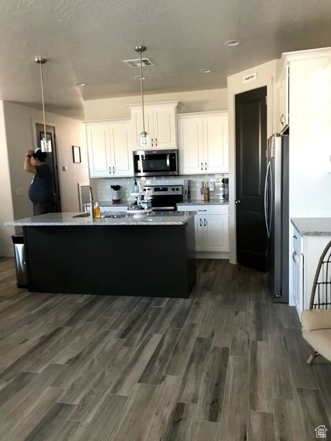 Kitchen with appliances with stainless steel finishes, white cabinetry, an island with sink, backsplash, and dark wood-style flooring