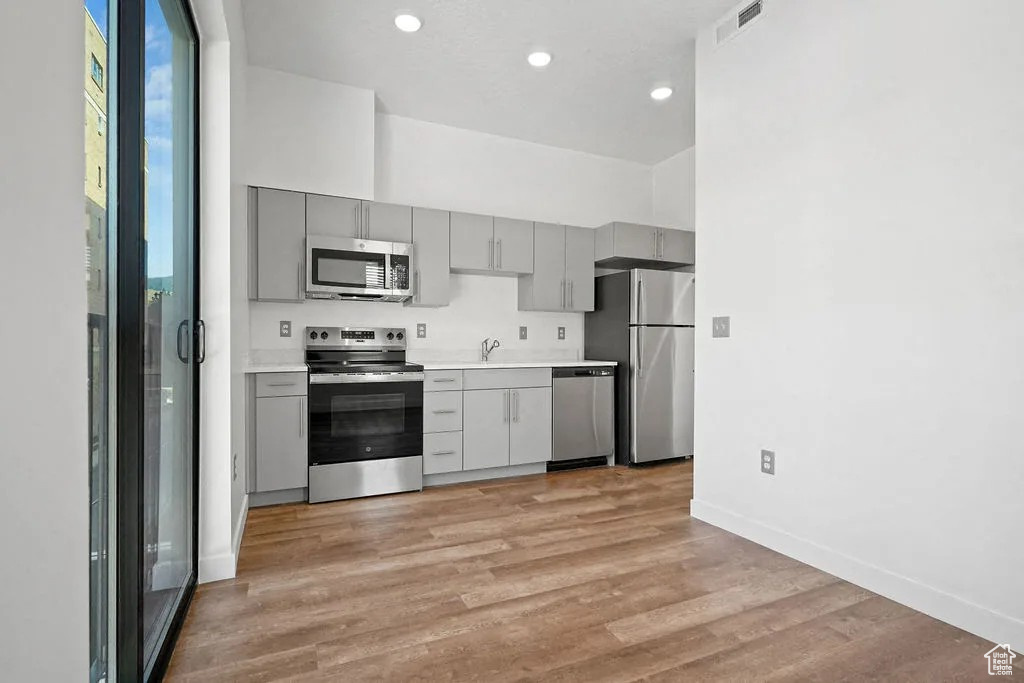 Kitchen featuring stainless steel appliances, gray cabinetry, light countertops, light wood finished floors, and recessed lighting
