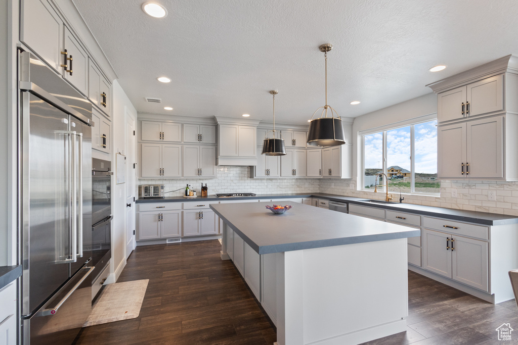 Kitchen with stainless steel appliances, backsplash, dark wood finished floors, a center island, and dark countertops