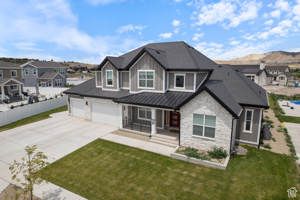 View of front of property with concrete driveway, stone siding, a porch, board and batten siding, and a standing seam roof