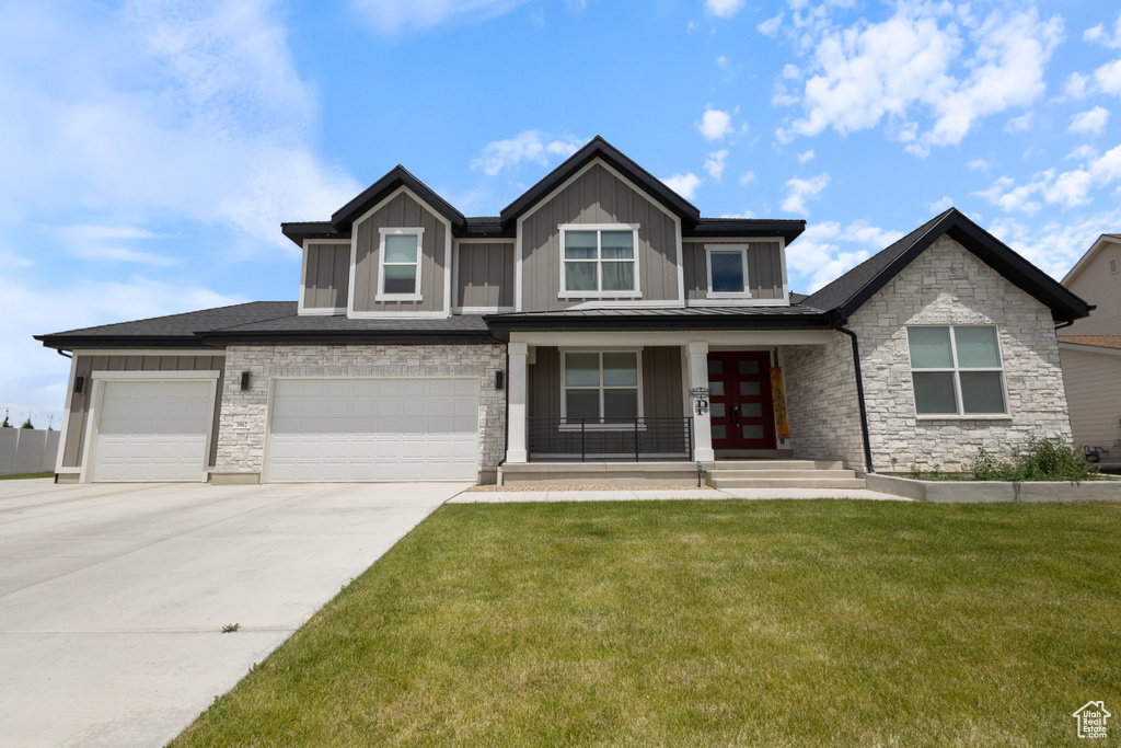 View of front of property featuring a front yard, a porch, driveway, stone siding, and board and batten siding
