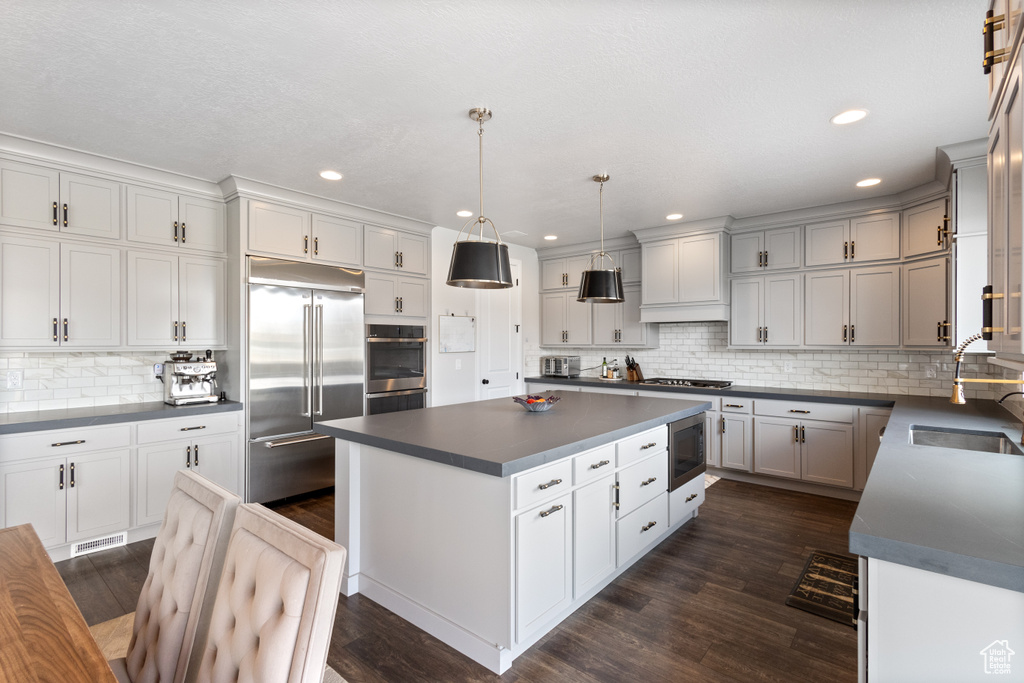 Kitchen with built in appliances, dark countertops, decorative backsplash, a kitchen island, and recessed lighting