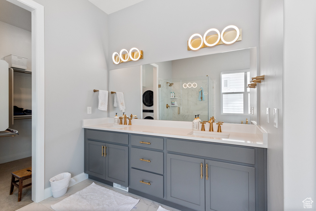 Full bath with stacked washer and clothes dryer, a stall shower, and double vanity