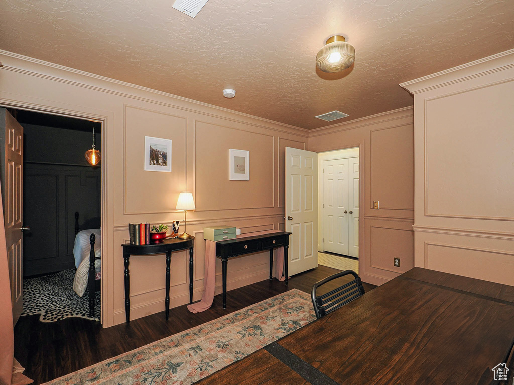 Office area with a decorative wall, dark wood-type flooring, and ornamental molding