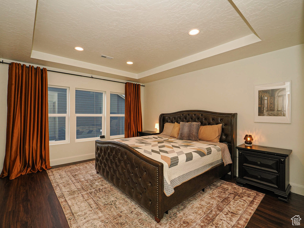 Bedroom with a raised ceiling, wood finished floors, recessed lighting, and a textured ceiling