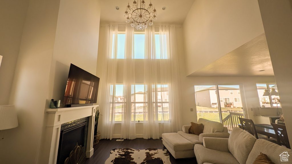 Living area featuring a high ceiling, a chandelier, plenty of natural light, and dark wood-style flooring