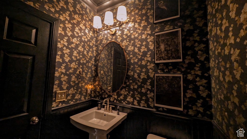 Half bathroom with wallpapered walls, crown molding, and a wainscoted wall