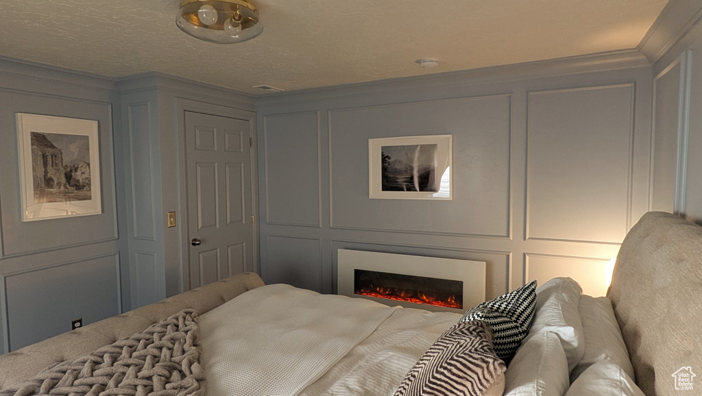 Bedroom featuring a decorative wall, a warm lit fireplace, and crown molding