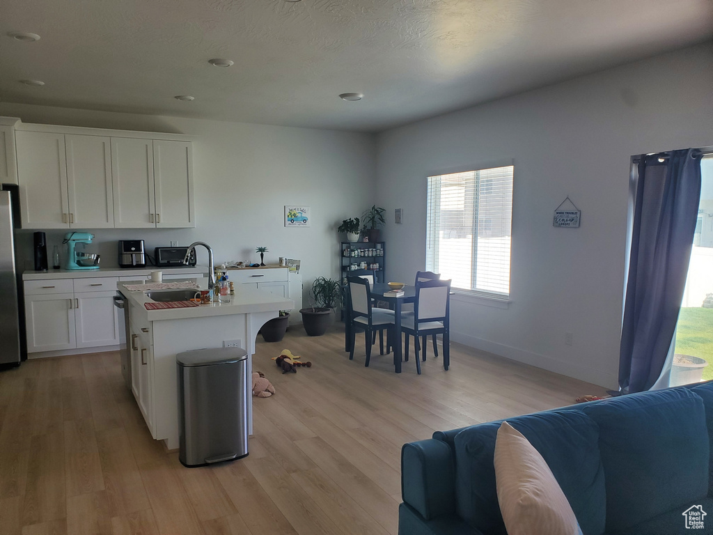 Kitchen featuring light wood-style floors, white cabinetry, light countertops, open floor plan, and a center island with sink
