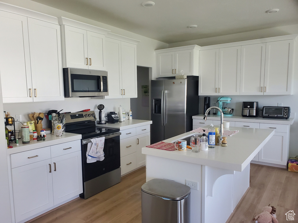 Kitchen featuring appliances with stainless steel finishes, light wood-type flooring, light countertops, and white cabinetry