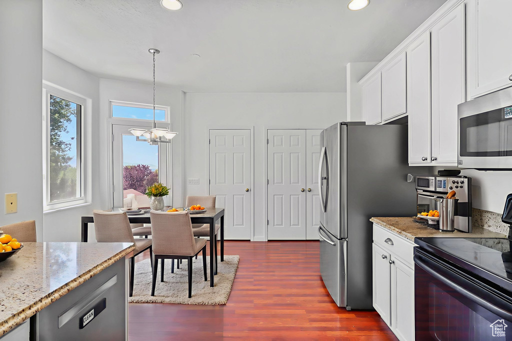 Kitchen featuring stainless steel appliances, dark wood-type flooring, a chandelier, light stone countertops, and white cabinets