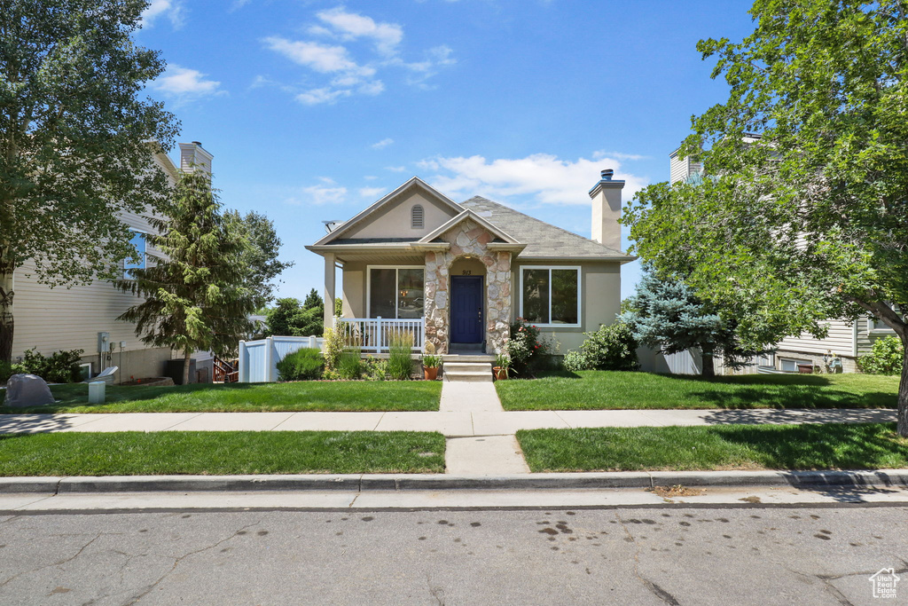 View of front of property featuring covered porch, a front yard, stone siding, and stucco siding