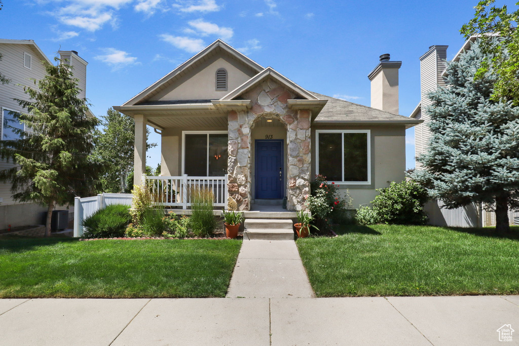 View of front facade with covered porch, stone siding, stucco siding, and a front yard