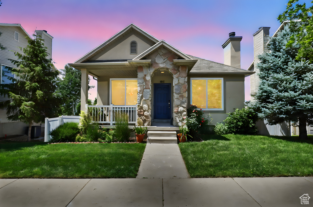 View of front of house with covered porch, stone siding, a yard, a chimney, and stucco siding