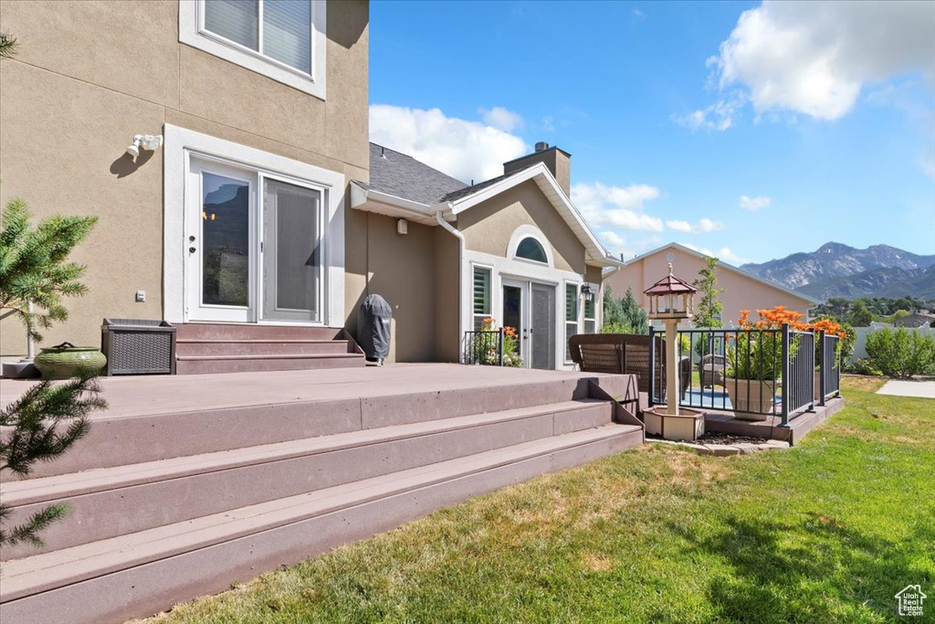 Rear view of property with stucco siding, a deck with mountain view, a yard, and a chimney
