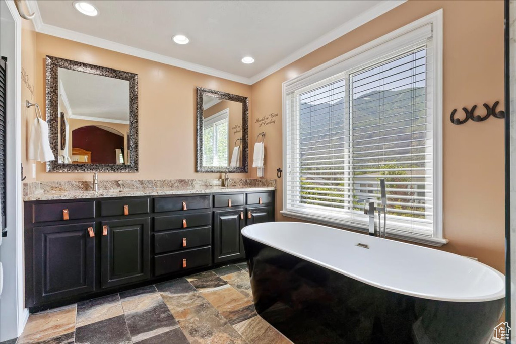 Full bathroom featuring double vanity, a soaking tub, crown molding, stone finish floors, and recessed lighting