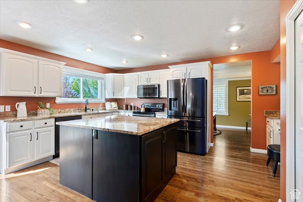 Kitchen with stainless steel appliances, white cabinetry, light wood-style flooring, a kitchen island, and light stone counters
