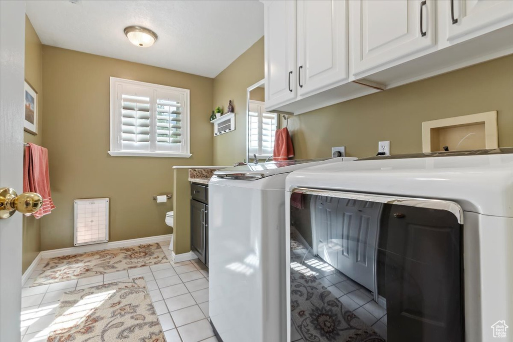 Laundry area featuring independent washer and dryer, light tile patterned floors, and cabinet space