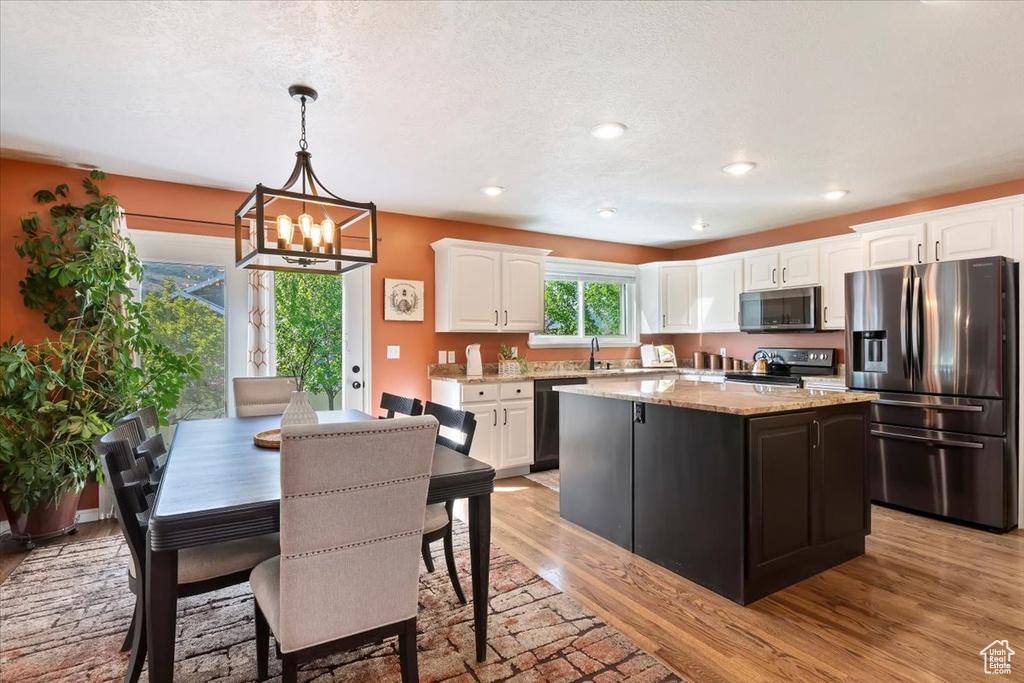 Kitchen featuring stainless steel appliances, white cabinets, a chandelier, light wood-style floors, and a center island