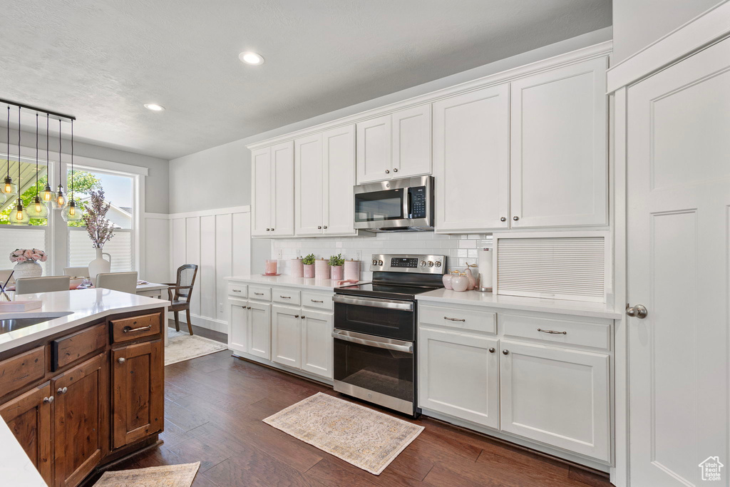 Kitchen featuring appliances with stainless steel finishes, light countertops, a wainscoted wall, white cabinets, and recessed lighting