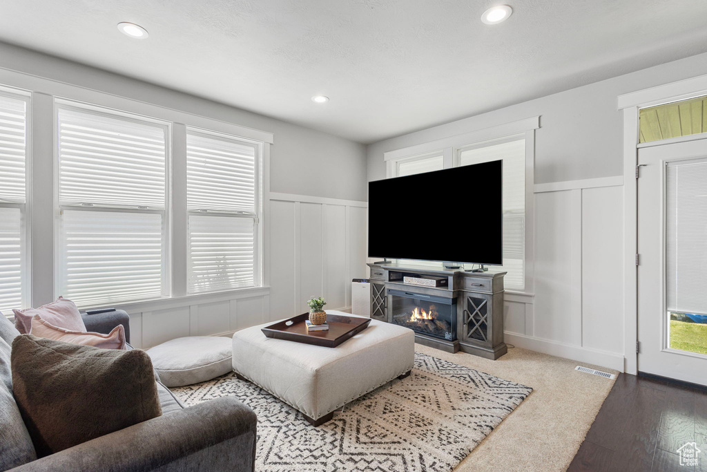 Living area with a decorative wall, wainscoting, wood finished floors, a glass covered fireplace, and recessed lighting