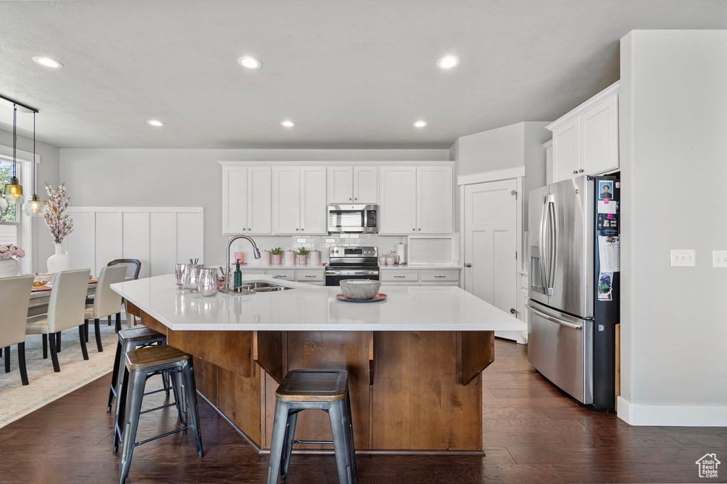 Kitchen featuring appliances with stainless steel finishes, an island with sink, light countertops, white cabinets, and recessed lighting