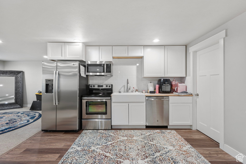 Kitchen featuring appliances with stainless steel finishes, backsplash, white cabinetry, wood finished floors, and recessed lighting