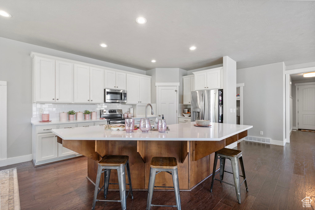 Kitchen with appliances with stainless steel finishes, a large island with sink, decorative backsplash, light countertops, and white cabinets