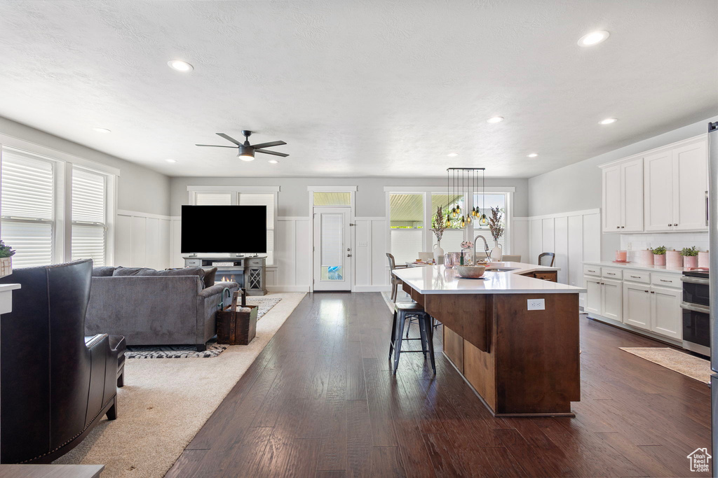Kitchen featuring ceiling fan, a wainscoted wall, white cabinets, light countertops, and a kitchen island with sink