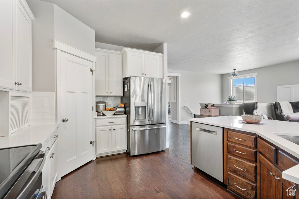 Kitchen with appliances with stainless steel finishes, dark wood-type flooring, light countertops, white cabinetry, and recessed lighting