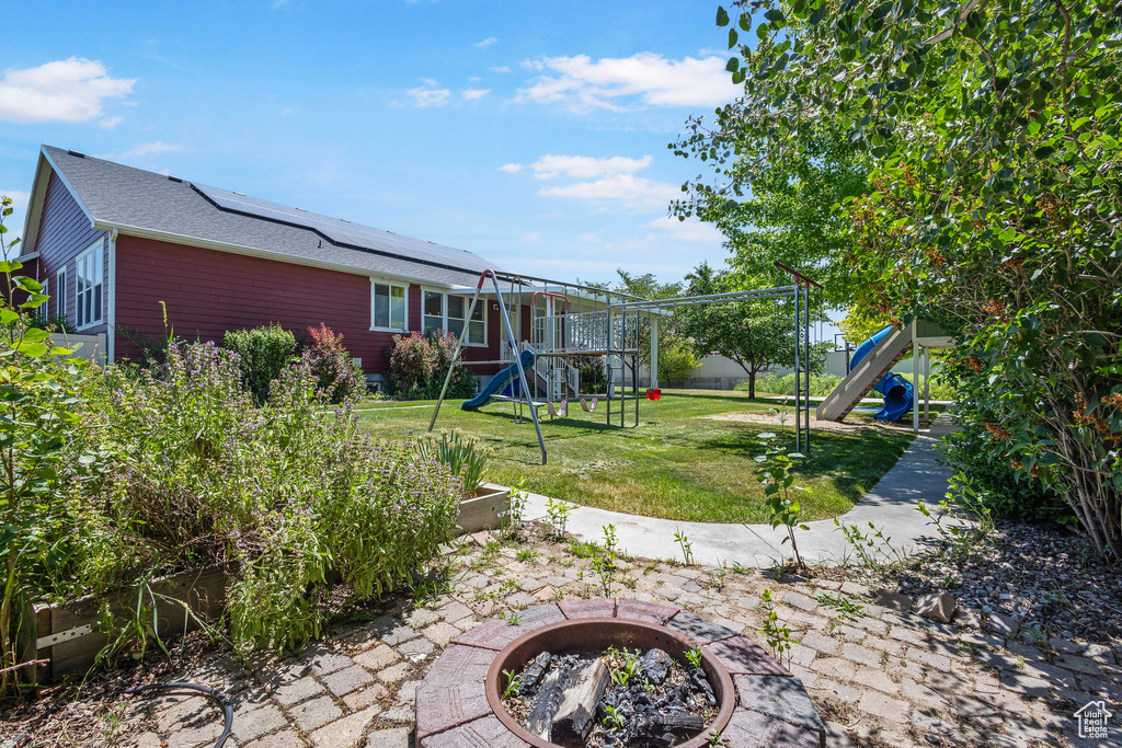 View of green lawn with a playground, a fire pit, and a vegetable garden