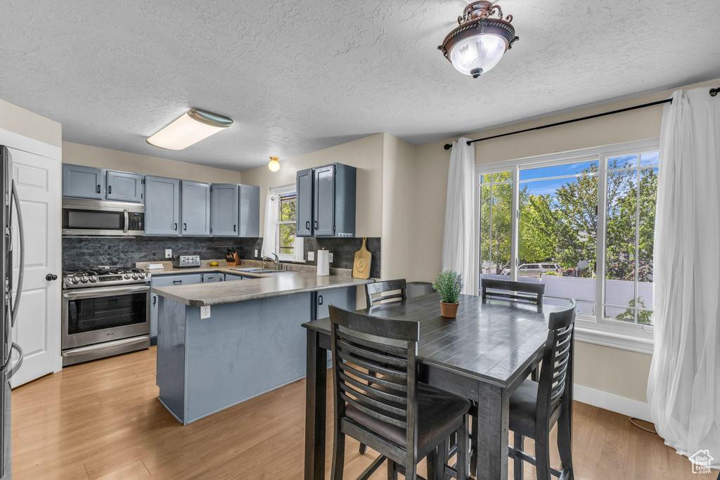 Kitchen featuring appliances with stainless steel finishes, a peninsula, decorative backsplash, a textured ceiling, and light wood-style flooring
