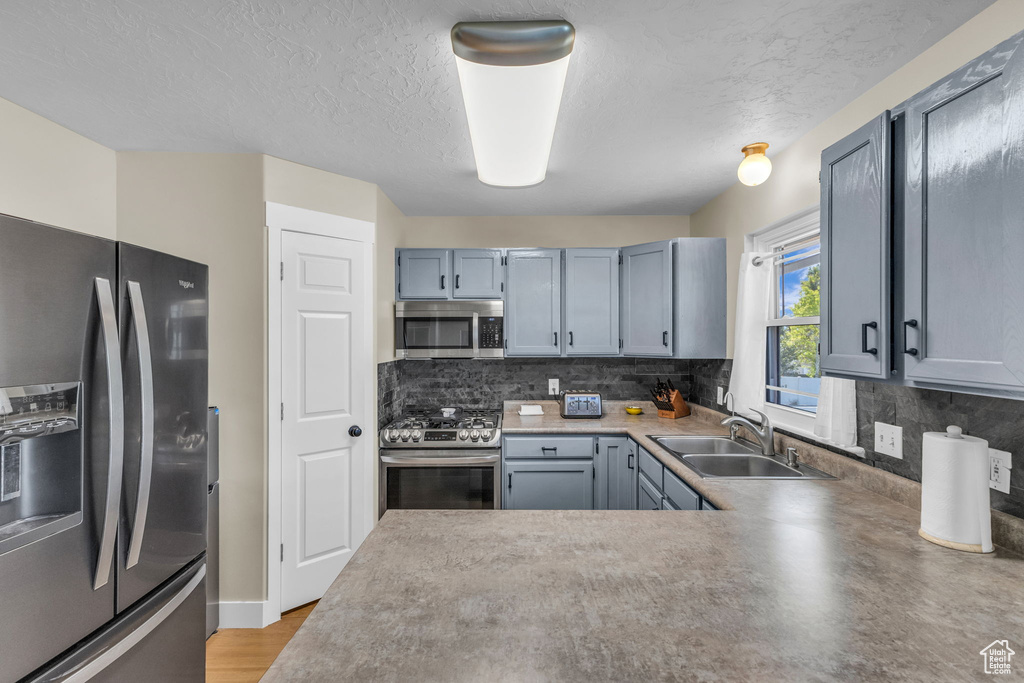 Kitchen with stainless steel appliances, decorative backsplash, a textured ceiling, and a peninsula