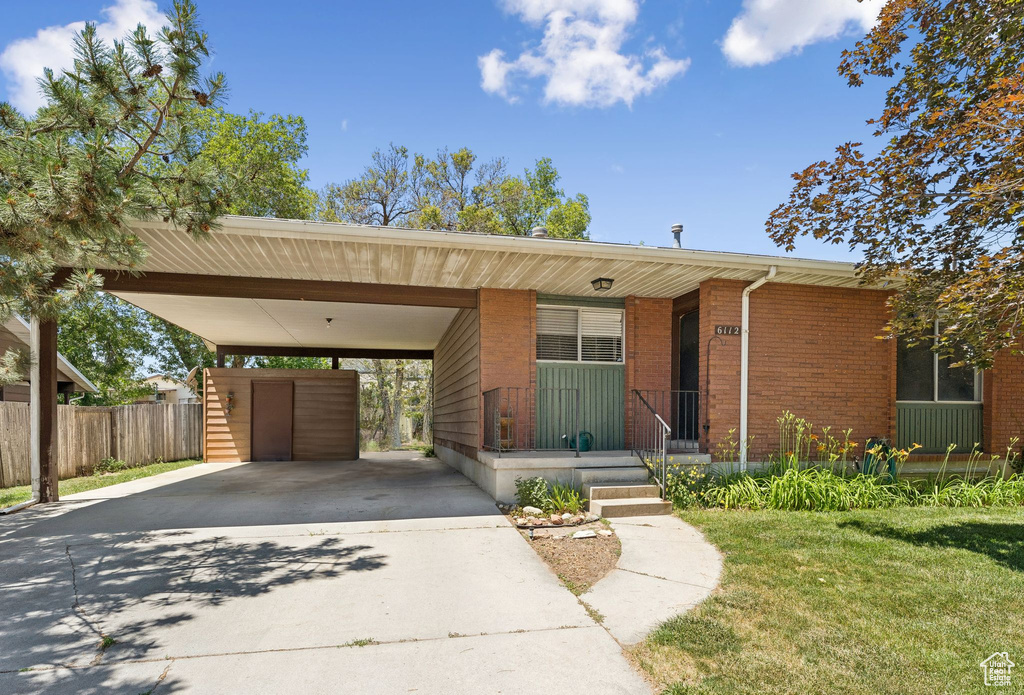 View of front of property featuring concrete driveway, brick siding, an attached carport, and covered porch