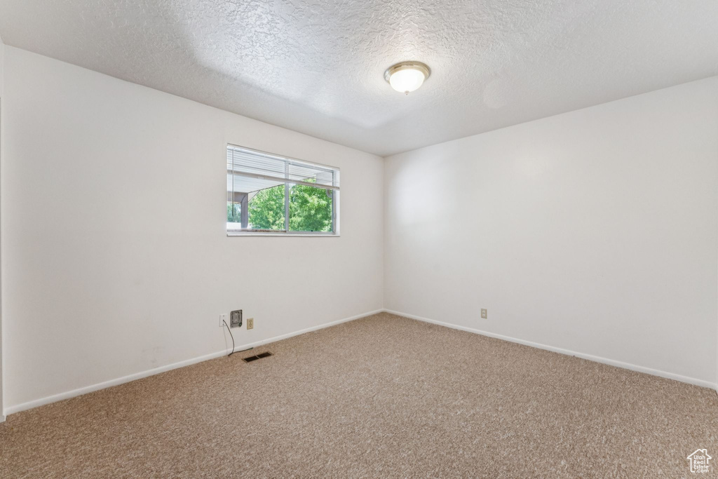 Carpeted spare room with a textured ceiling and baseboards