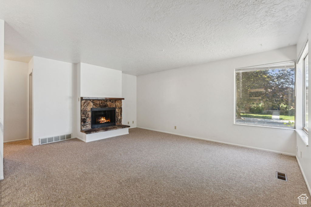 Unfurnished living room featuring plenty of natural light, carpet flooring, a textured ceiling, and a stone fireplace