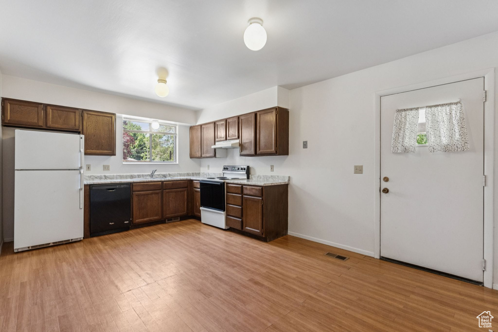 Kitchen with white appliances, under cabinet range hood, light countertops, and light wood finished floors