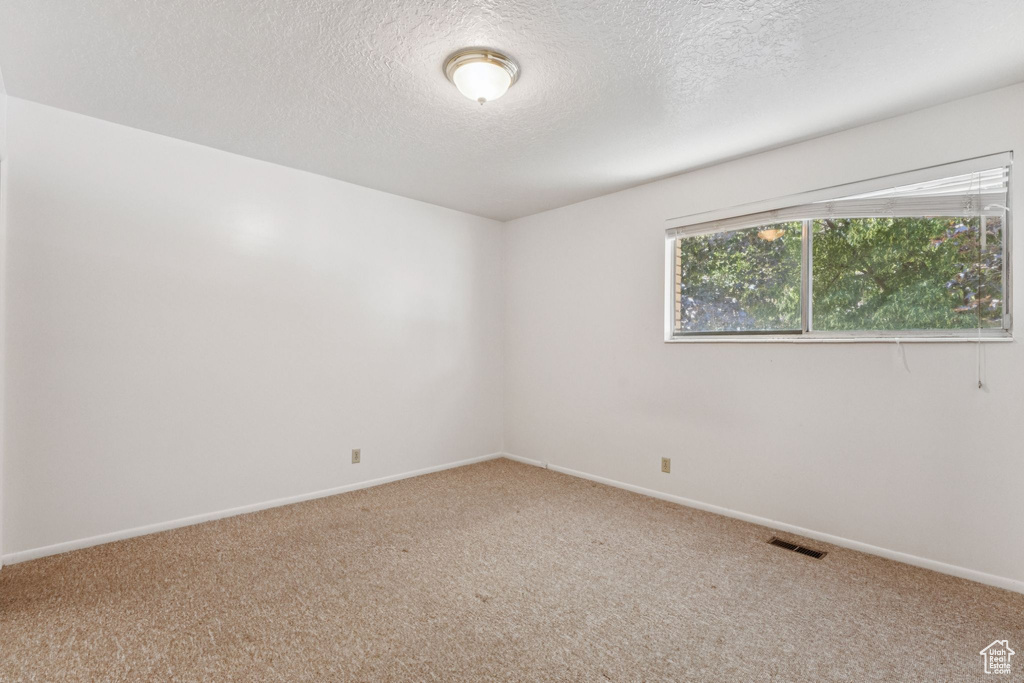 Carpeted empty room featuring a textured ceiling and baseboards