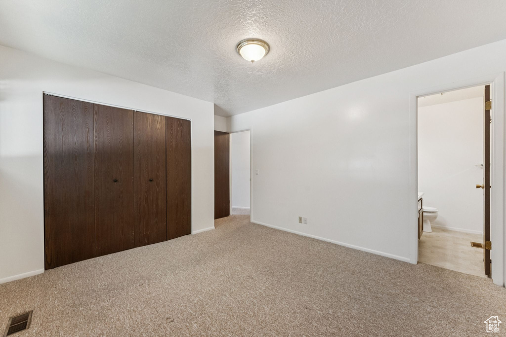 Unfurnished bedroom with light carpet, a closet, a textured ceiling, and connected bathroom