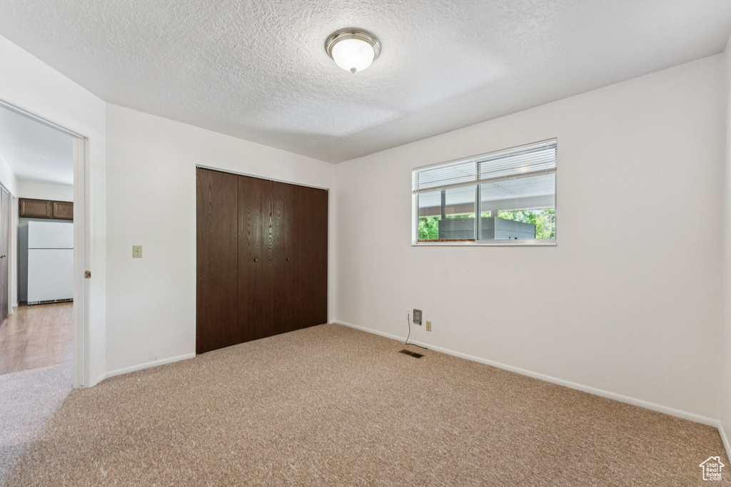 Unfurnished bedroom with freestanding refrigerator, light carpet, a closet, and a textured ceiling