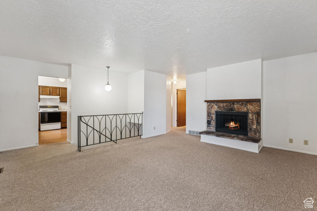 Unfurnished living room featuring light carpet, a fireplace, and a textured ceiling